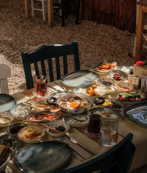 Masaya yayılmış çok çeşitli küçük tabaklarla serpme kahvaltı, yanında çay bardakları